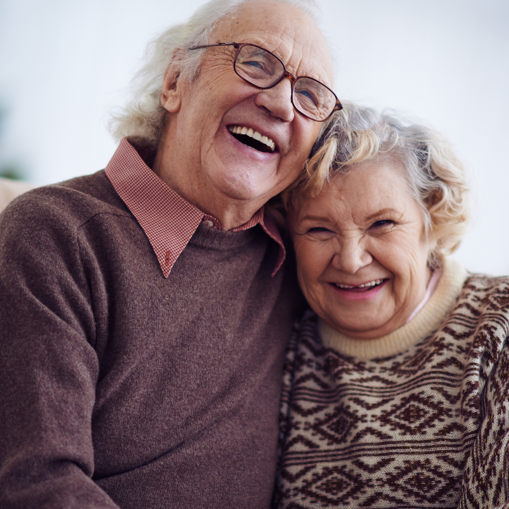 Two elderly people smiling and hugging.