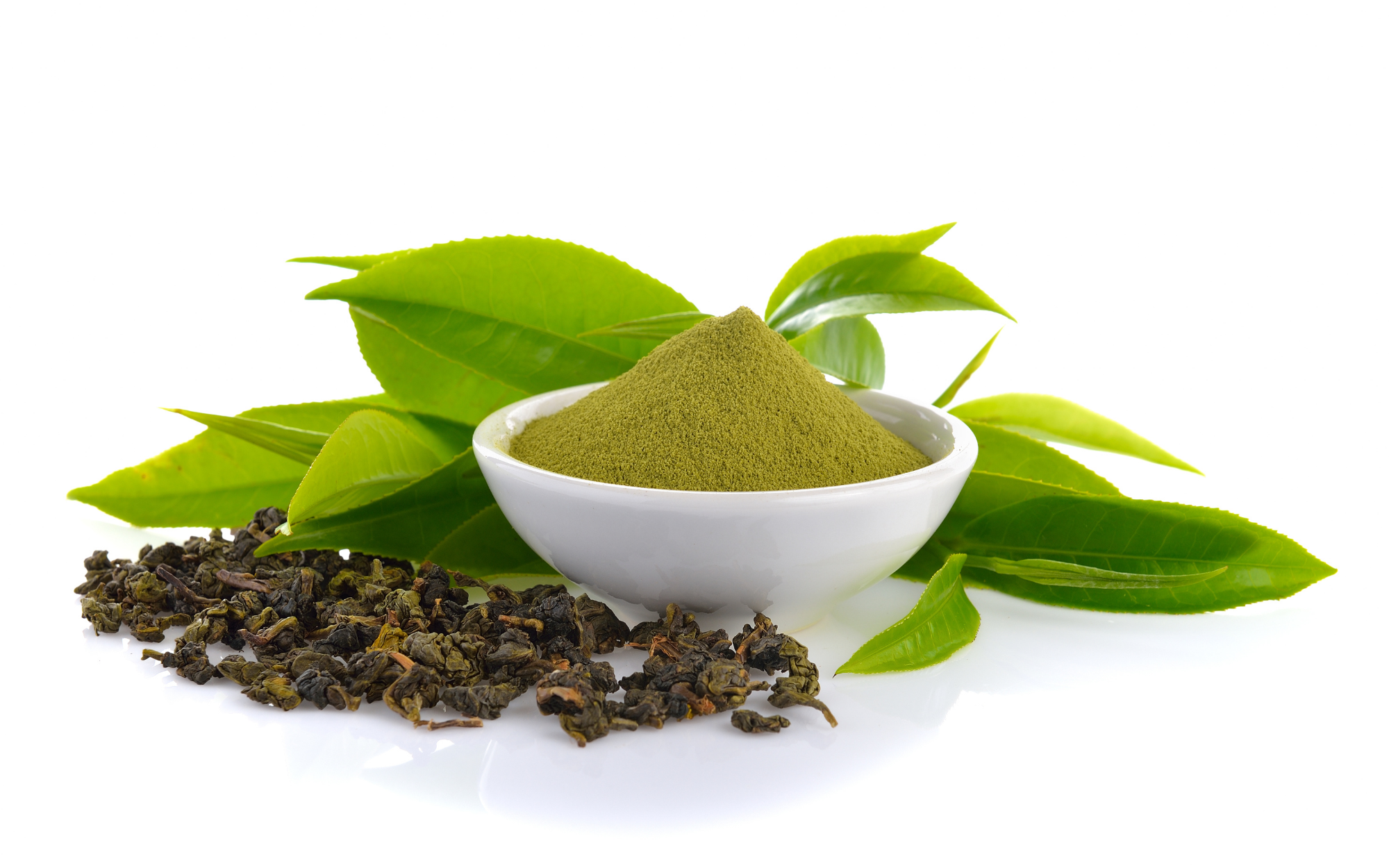 Bowl of green powder with fresh leaves and dried tea leaves.