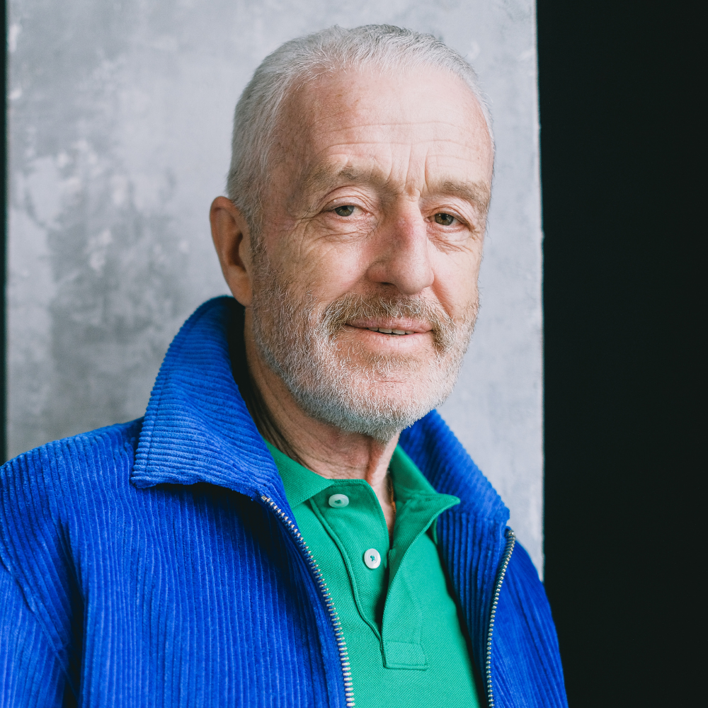 Man with gray hair and beard wearing blue jacket and green shirt.