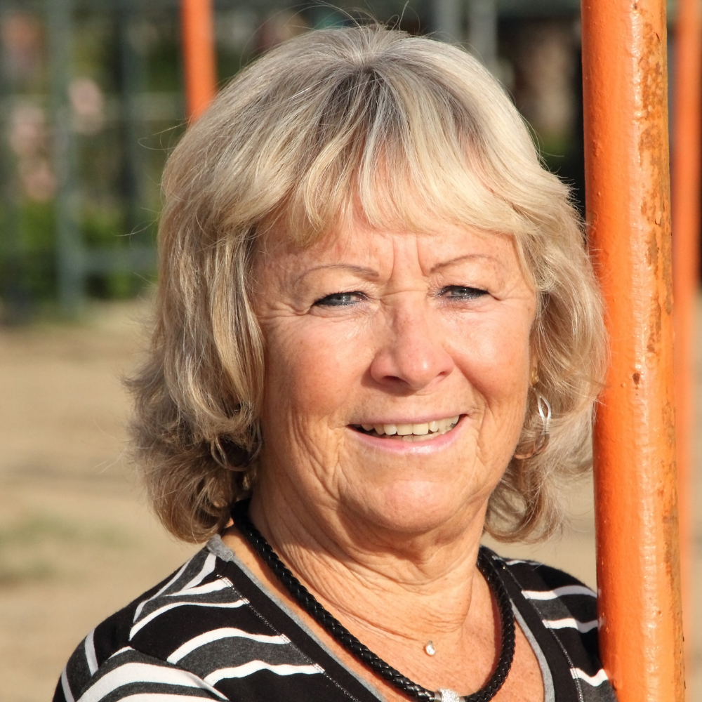 Smiling older woman with short blonde hair, standing near an orange post outdoors.