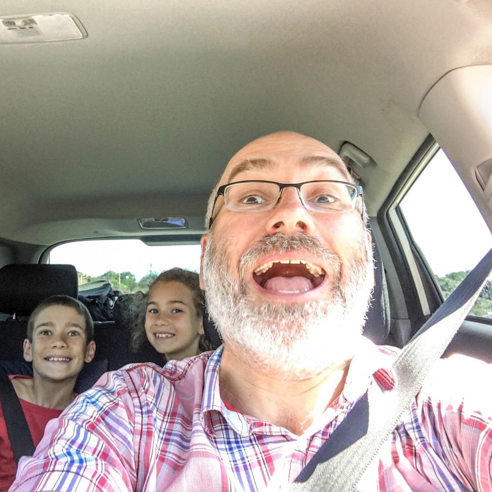 A man and two children smiling in a car, wearing seatbelts.