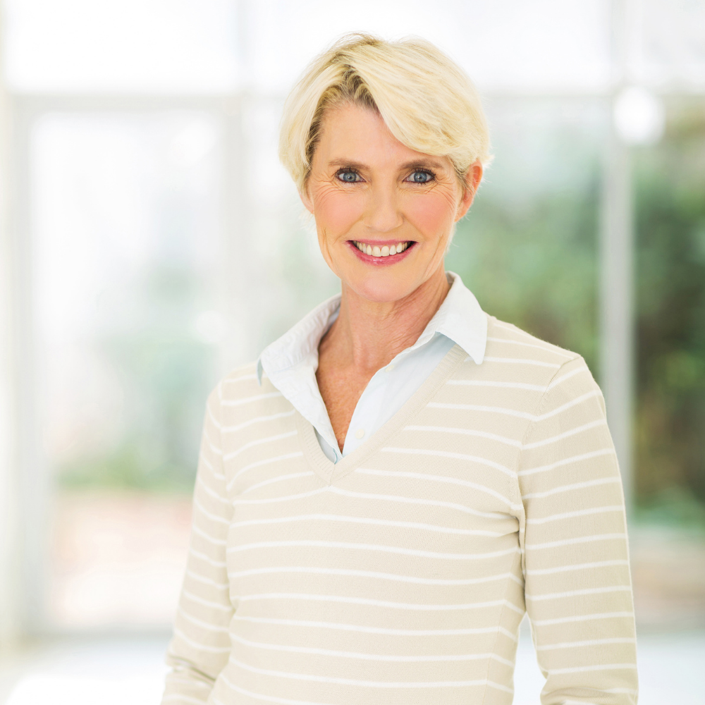 Smiling person with short blonde hair wearing a striped sweater in a bright setting.