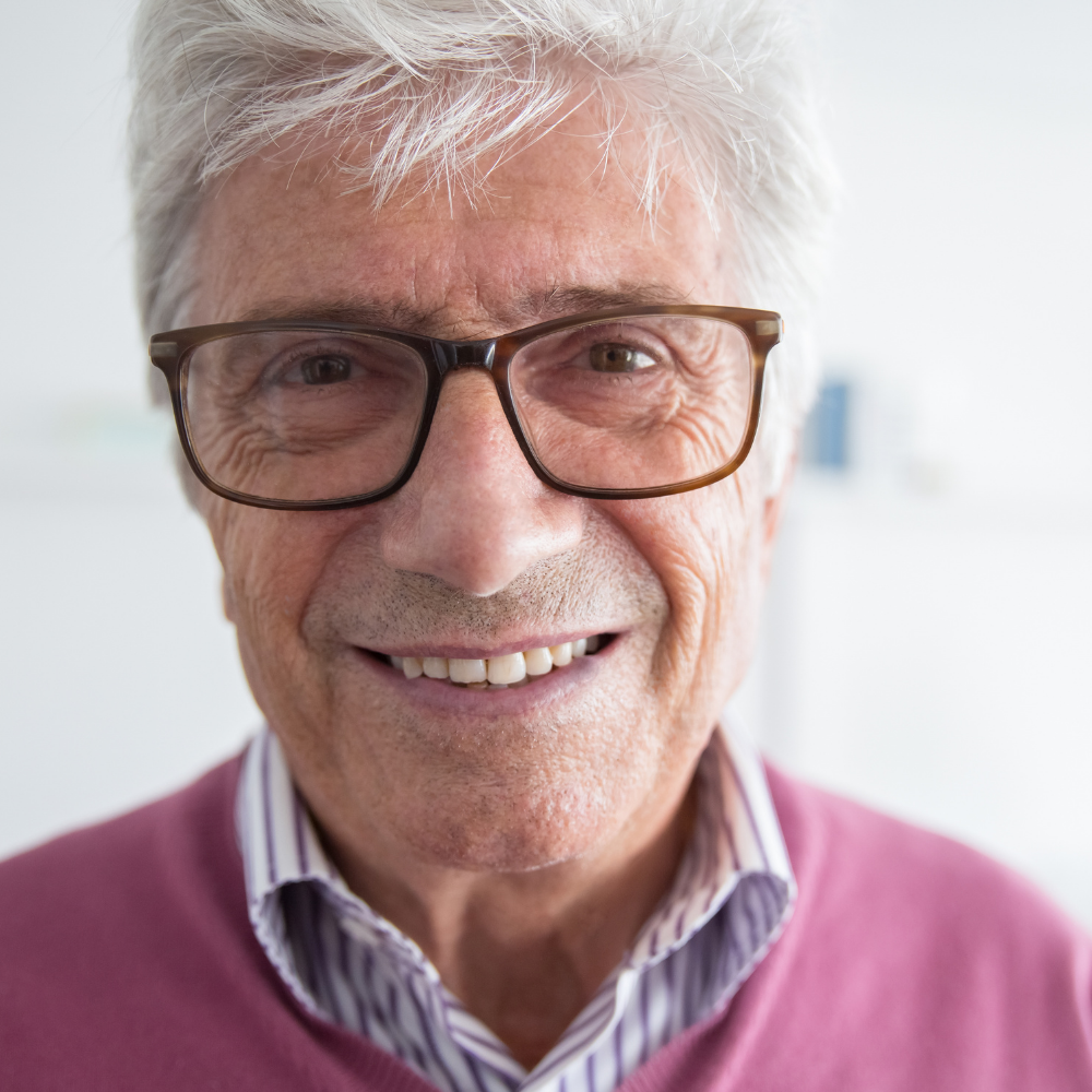 Elderly man with glasses smiling at the camera.