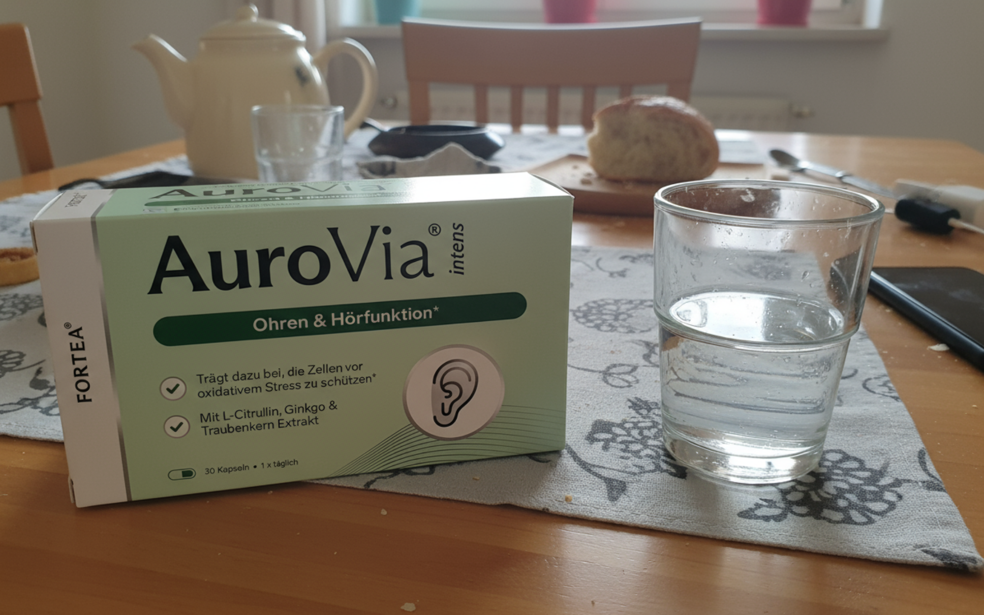 A box of AuroVia capsules and a glass of water on a table.