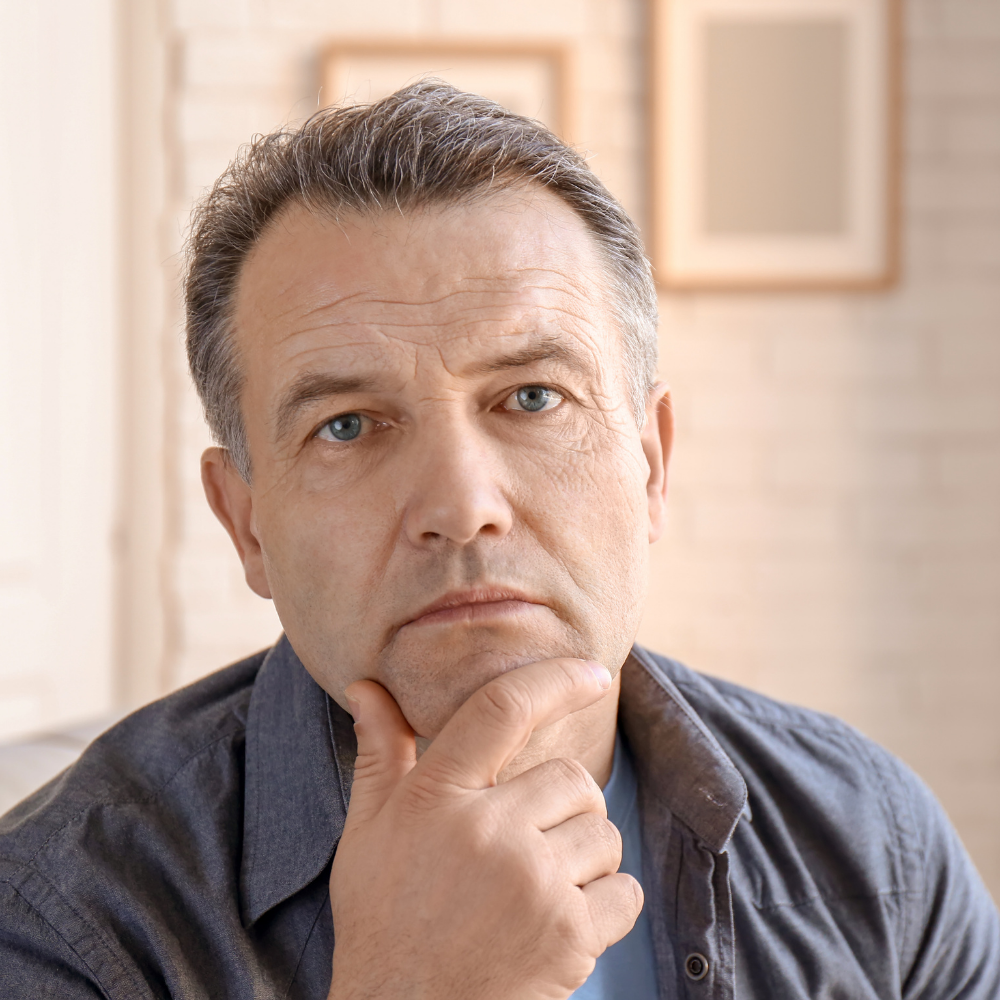 Man with thoughtful expression, hand on chin, in a softly lit room.