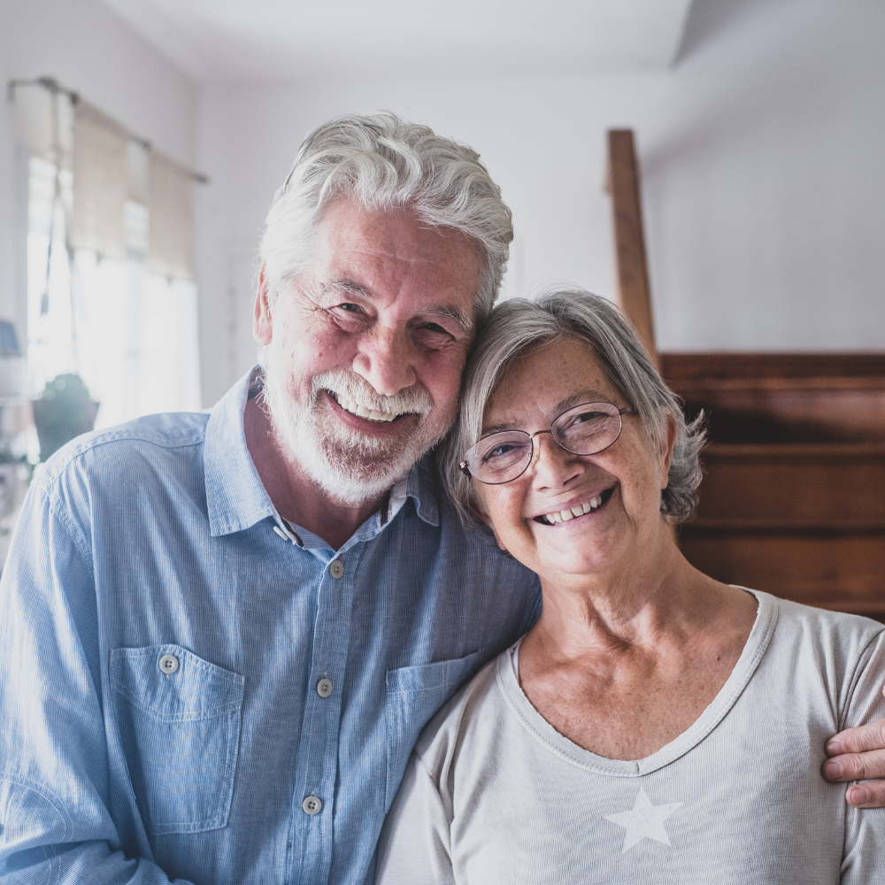 Smiling older couple embracing indoors by a staircase.