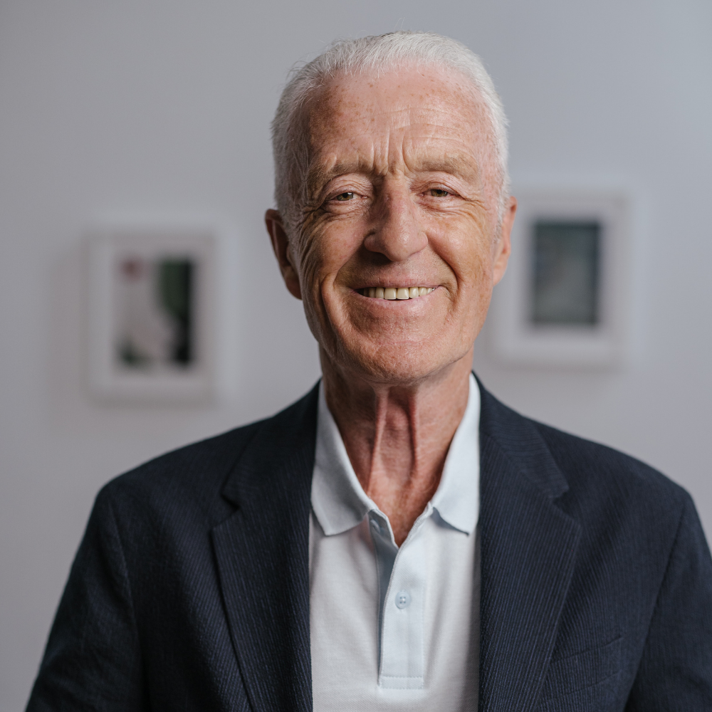 Elderly man smiling in a suit with blurred art in the background.