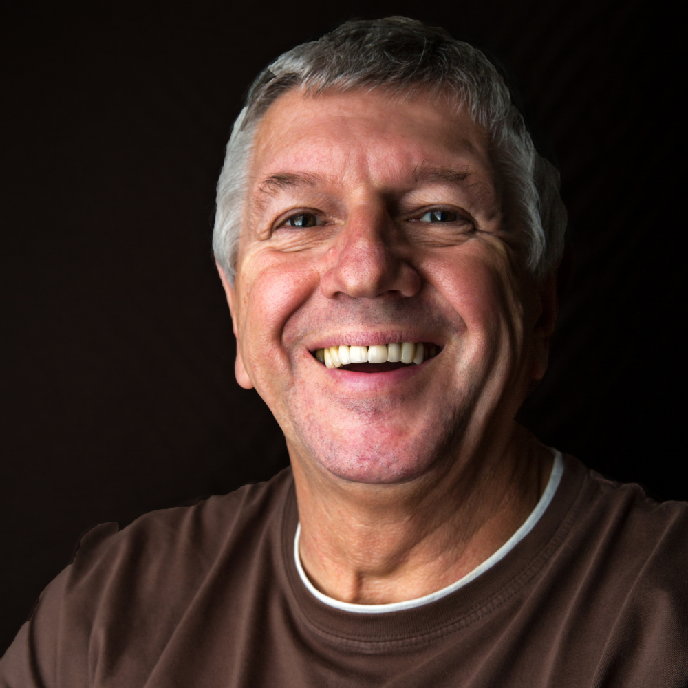 Smiling man in a brown shirt against a dark background.