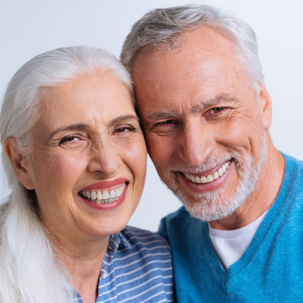 Smiling older couple with gray hair close together against a light background.