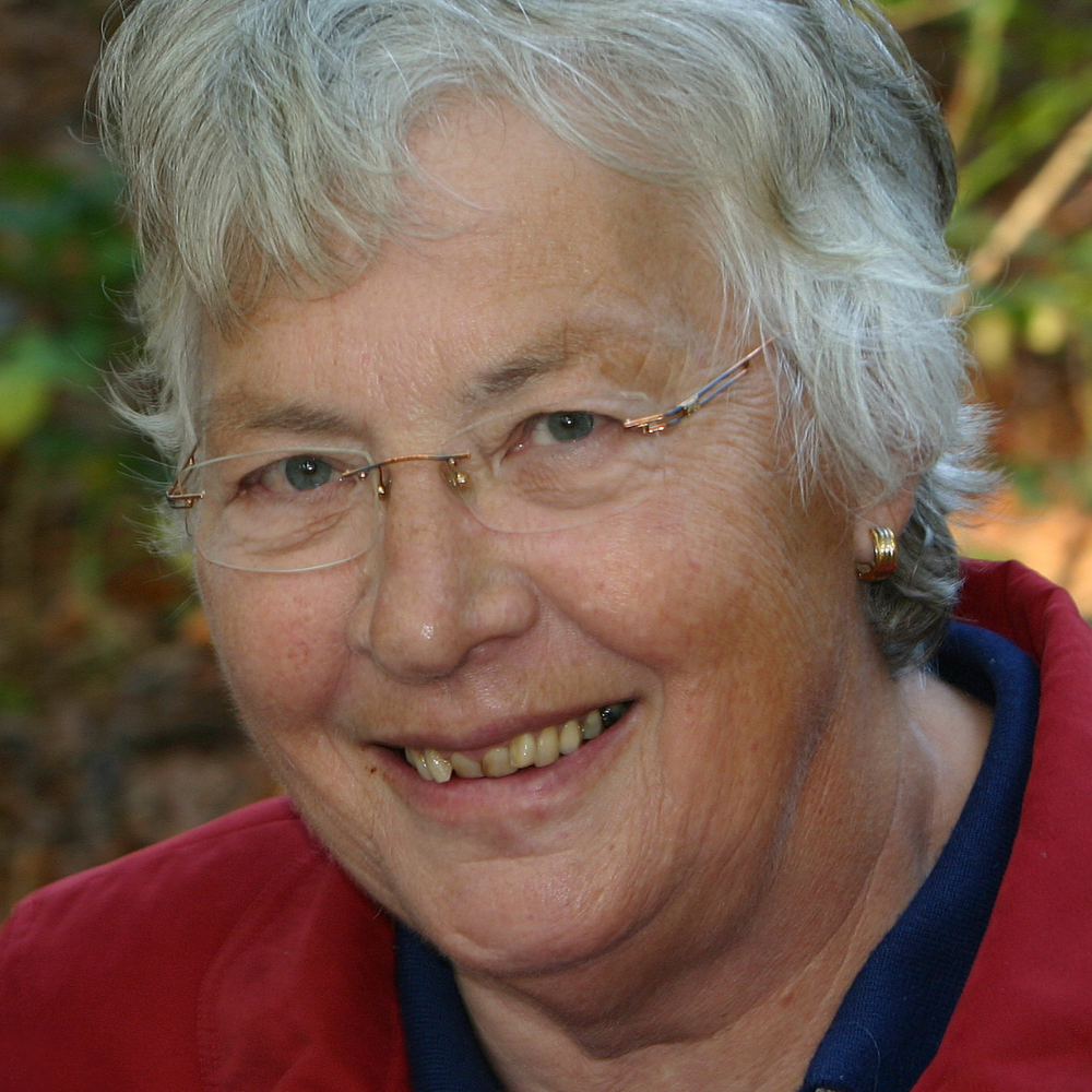 Smiling person with short gray hair and glasses outdoors.