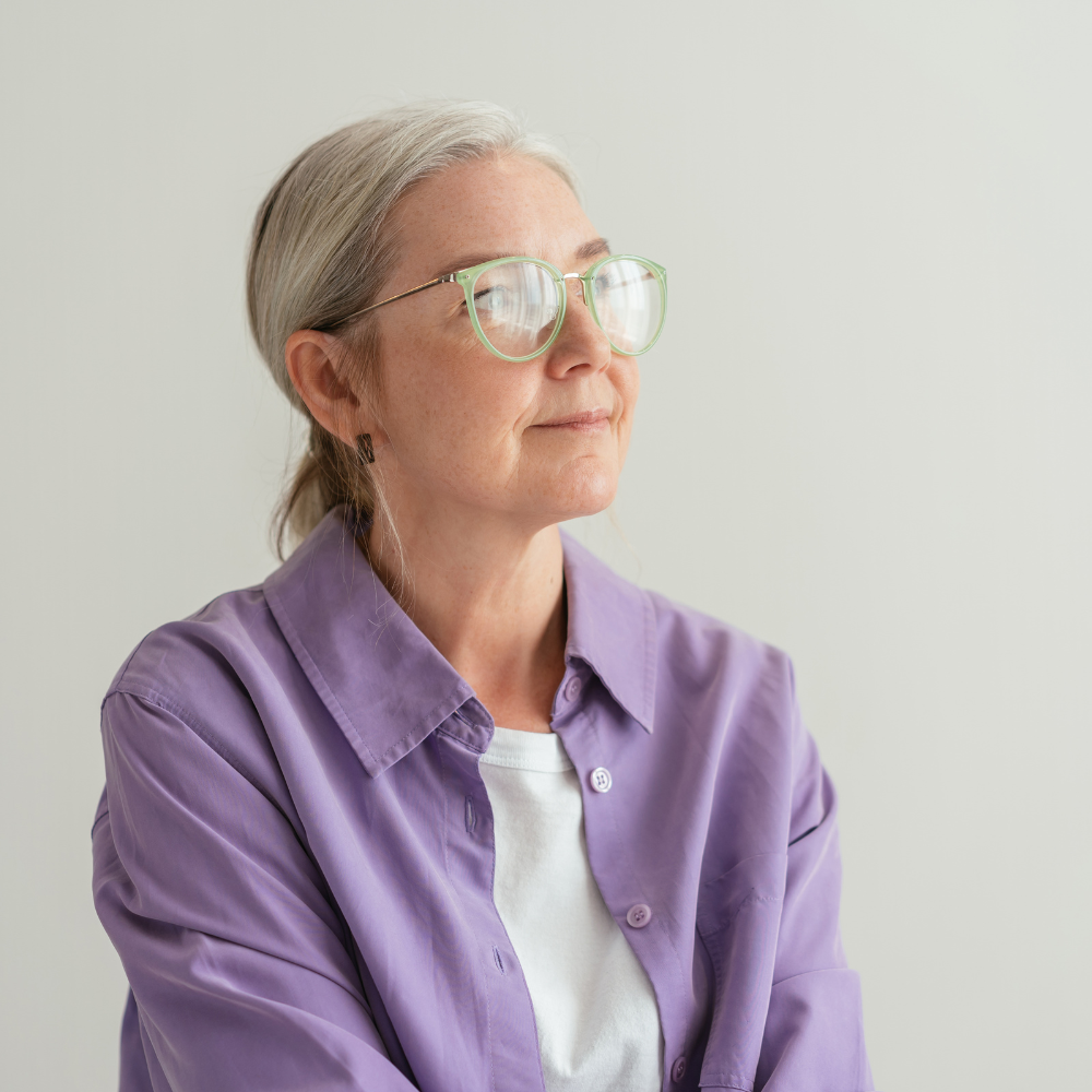 Woman with glasses wearing purple shirt, looking to the side.