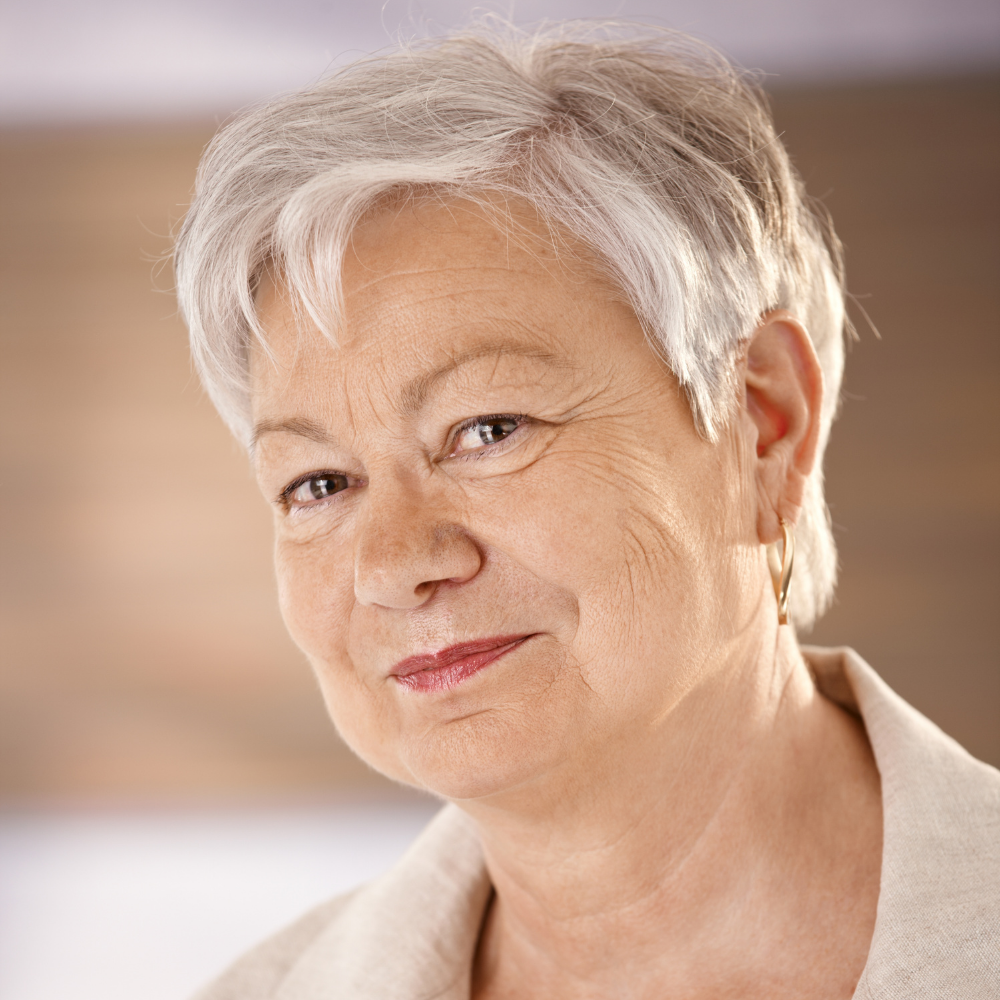 Older woman with short grey hair, smiling slightly, wearing earrings.