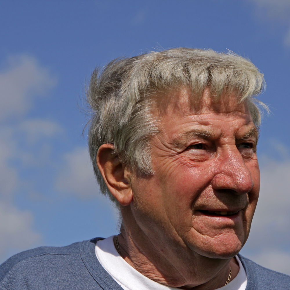 Older man smiling against a blue sky background.