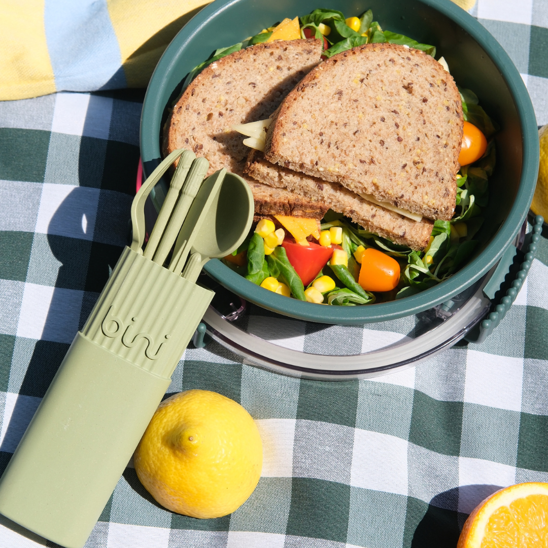 Sandwich and salad in a bowl with utensils on a checkered tablecloth.