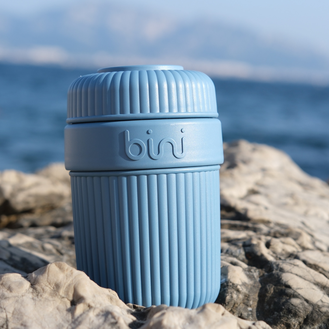 Blue ribbed container labeled 'bini' on a rock by the sea.