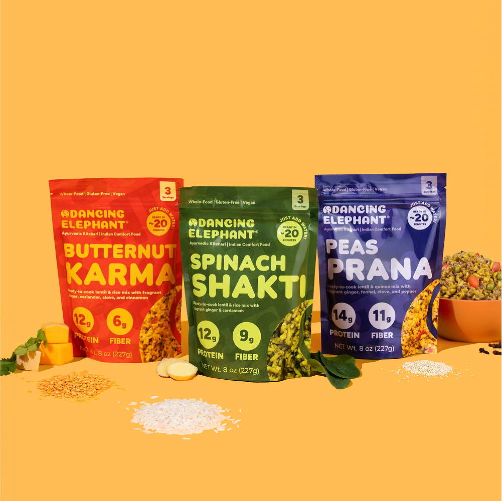 Three colorful food packages labeled Butternut Karma, Spinach Shakti, and Peas Prana on an orange background.