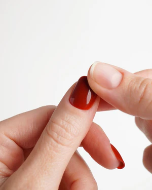A close-up of a person applying a red, glossy press-on nail to their finger.