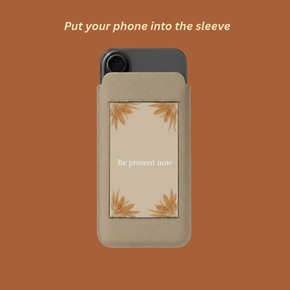 Phone in a beige sleeve with text 'Be present now' and floral design.