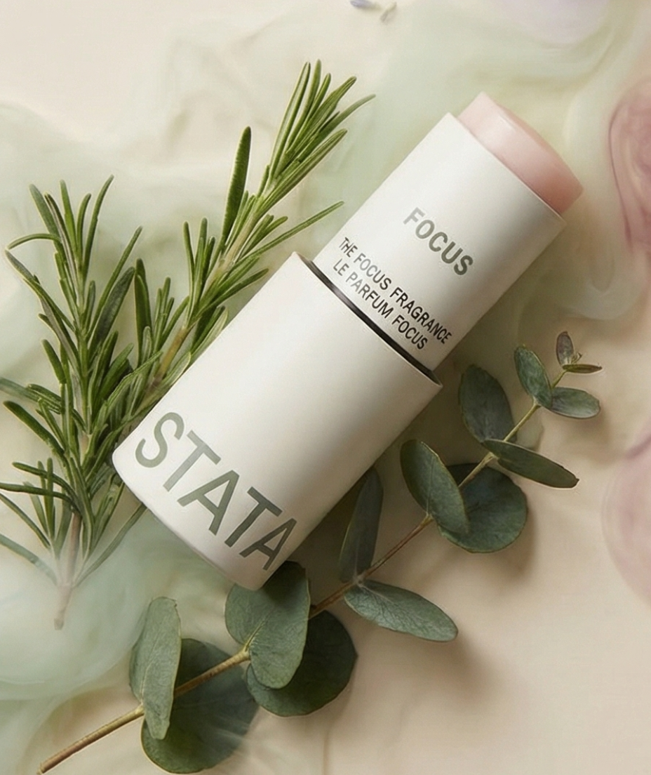 A white tube of Stata Focus solid fragrance stick is arranged with sprigs of rosemary and eucalyptus.