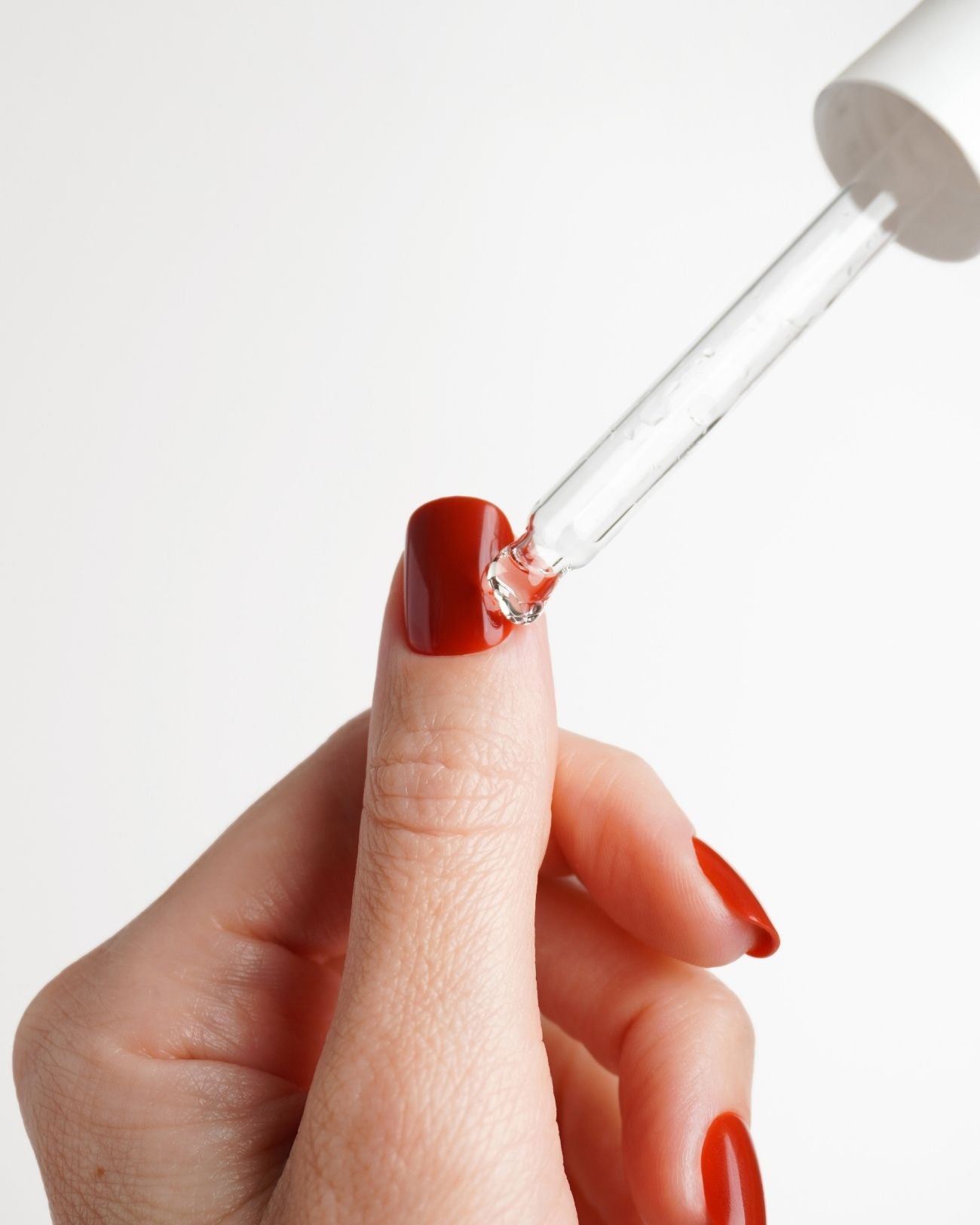 A person using a wooden stick to apply a substance to the inside of a red artificial nail.