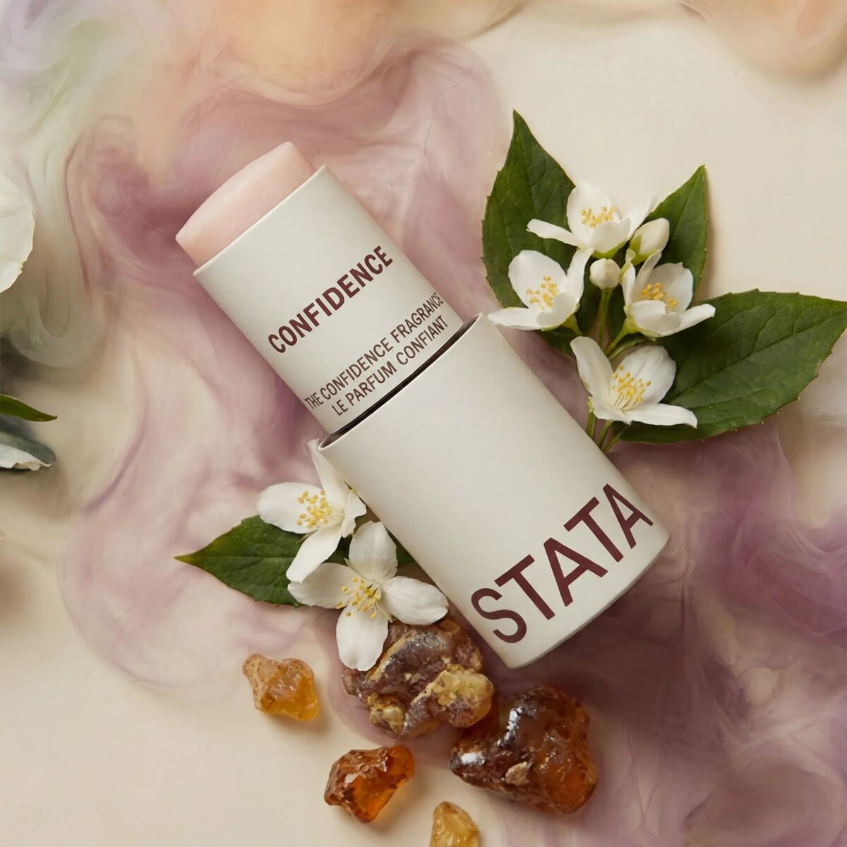 An open tube of Stata Confidence solid fragrance, surrounded by jasmine flowers and amber resin.