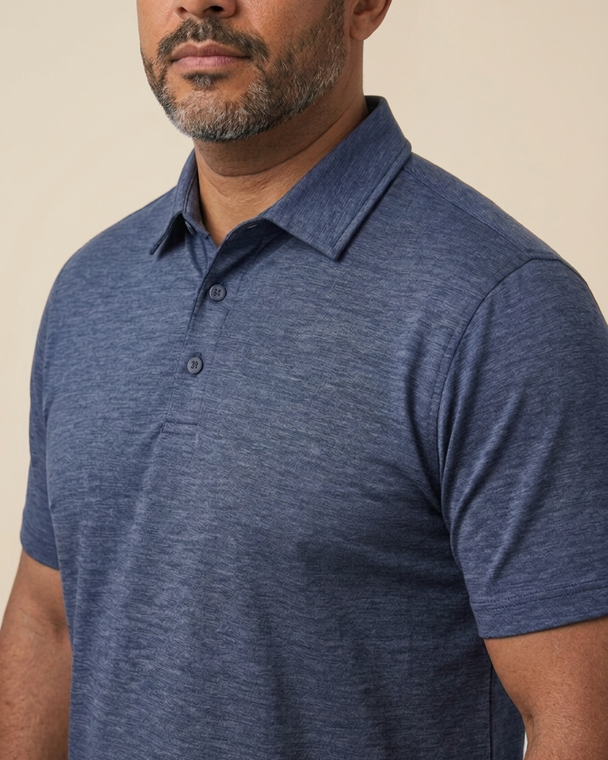 A close-up of a man with a salt-and-pepper beard wearing a blue heathered polo shirt.