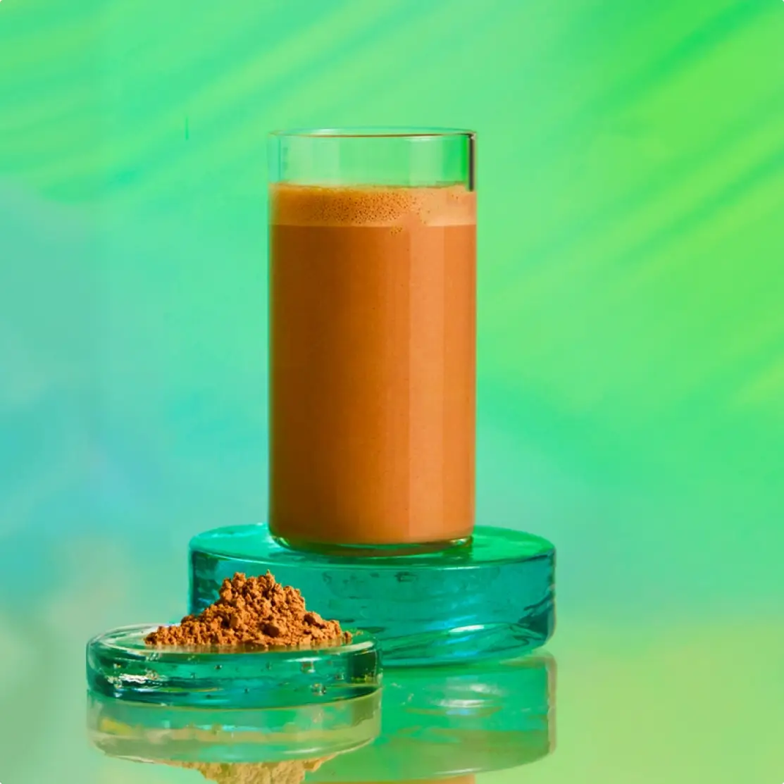 A tall glass of a brown beverage with a small dish of brown powder against a vibrant green background.