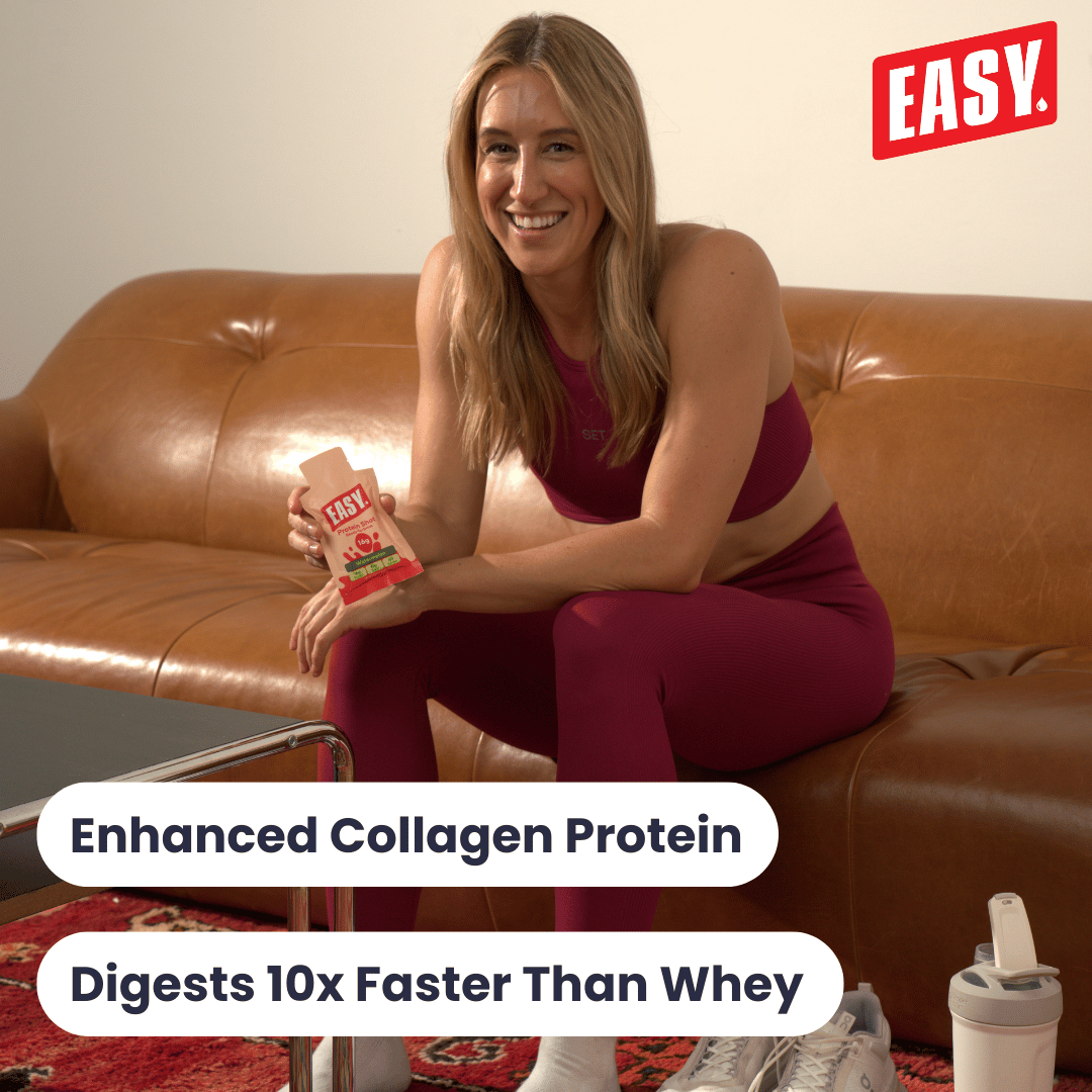 Smiling woman in workout clothes holding a protein drink on a brown sofa.
