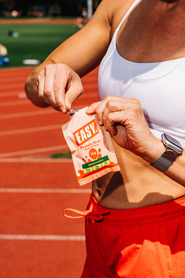 Person opening a protein shot packet on a running track.
