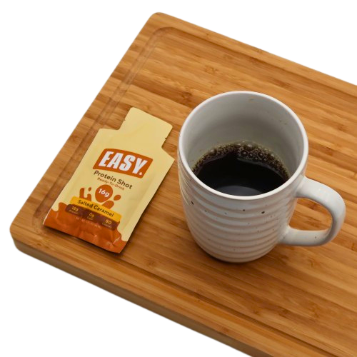 White mug of black coffee and protein shot on wooden tray.