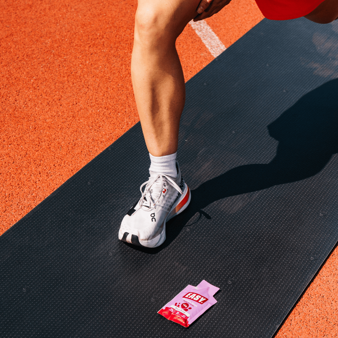 Person stretching on track with energy gel packet on mat.