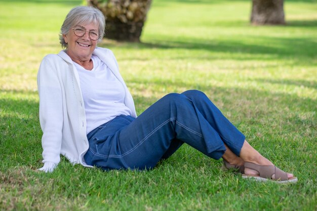 Elderly woman smiling while sitting on grass in a park.