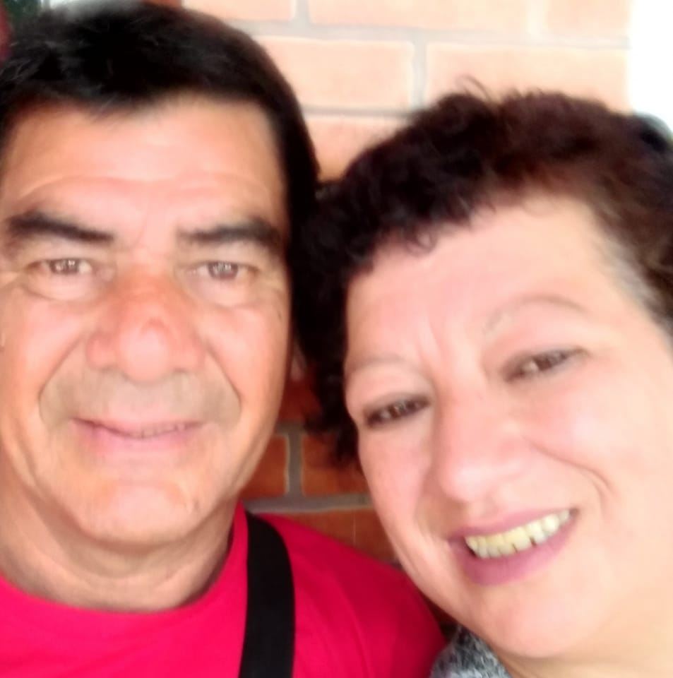 Two people smiling, with a brick wall in the background.