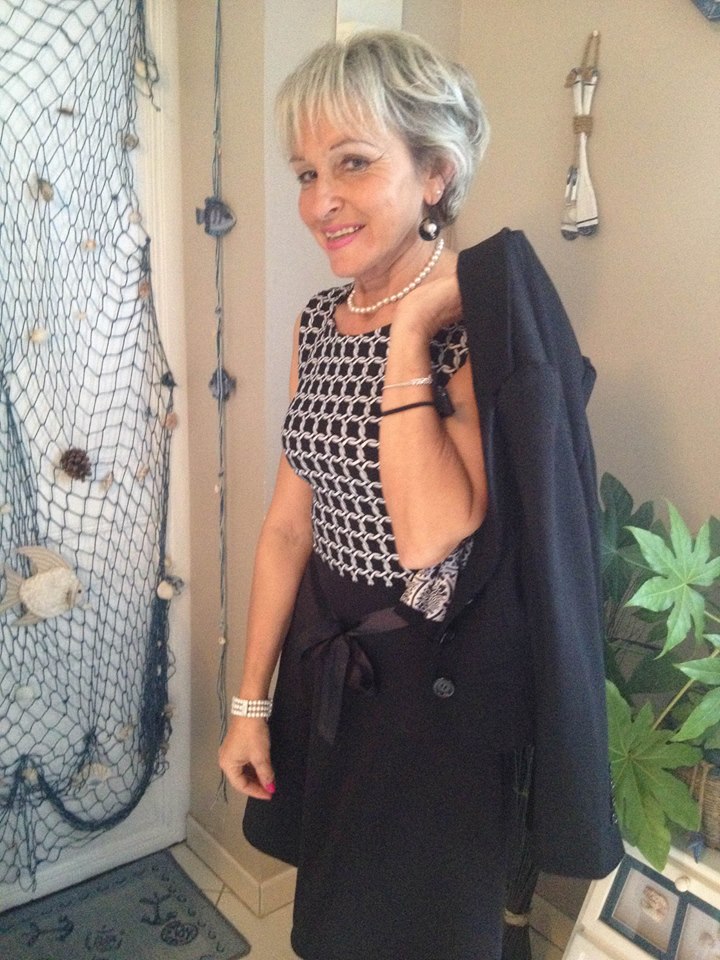 Woman in a patterned dress holding a coat, next to a decorative net and plants.