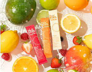 Assorted fruits and three colorful drink packets arranged on a white surface.