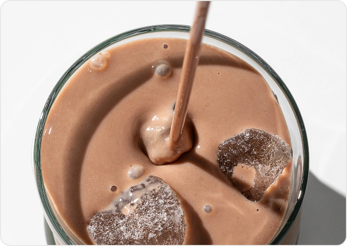 Glass of chocolate milkshake with ice cubes and straw.