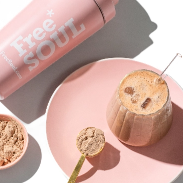 Pink shaker bottle, glass of iced coffee, and protein powder on a pink plate.
