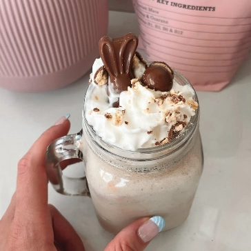 A hand holding a milkshake topped with whipped cream, chocolate, and crumbled cookies in a mason jar.