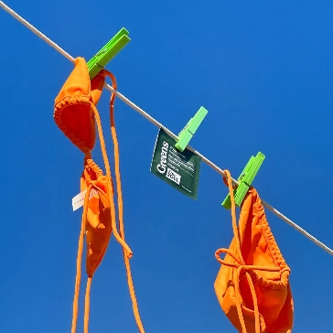 Orange fabric pieces clipped to a clothesline with green pegs against a blue sky.
