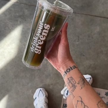 Person holding a clear tumbler with green juice and text 'drink your greens.'