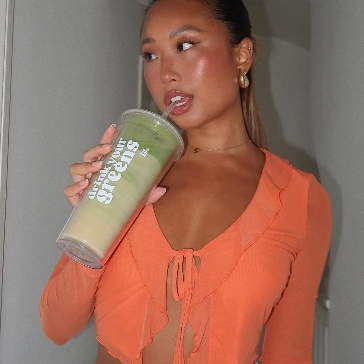 Person in orange top holding a large drink cup.