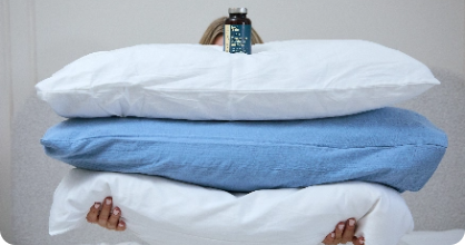 Person holding three pillows with a bottle on top.