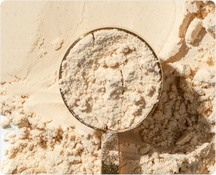 A measuring scoop filled with beige powder on a pile of the same powder.