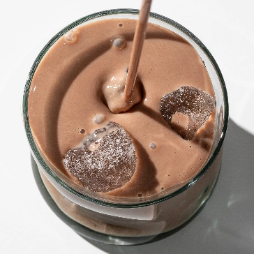 Glass of chocolate milk with ice cubes and a straw.