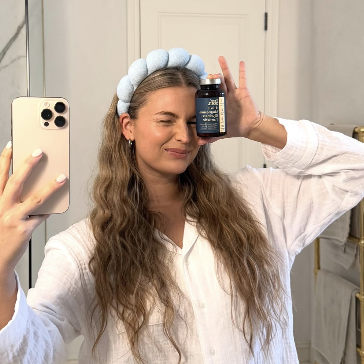Person taking a mirror selfie holding a bottle, wearing a white shirt and blue headband.