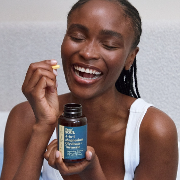 Person smiling, holding a supplement bottle and a pill.