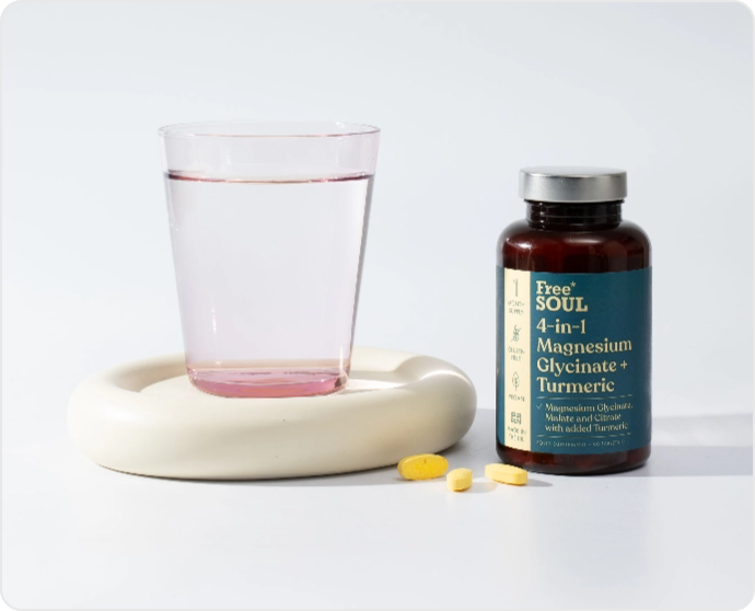Glass of pink liquid and supplement bottle with yellow pills on a white surface.