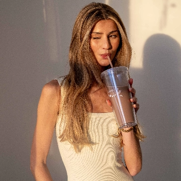 Woman in white dress drinking from a large cup with a straw.