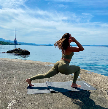 Person doing yoga on a mat by the sea with a smokestack in the background.