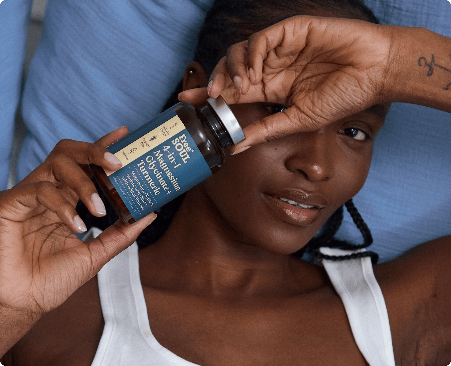 Person holding a bottle labeled '4-in-1 Magnesium Glycinate + Turmeric' while lying on a blue pillow.